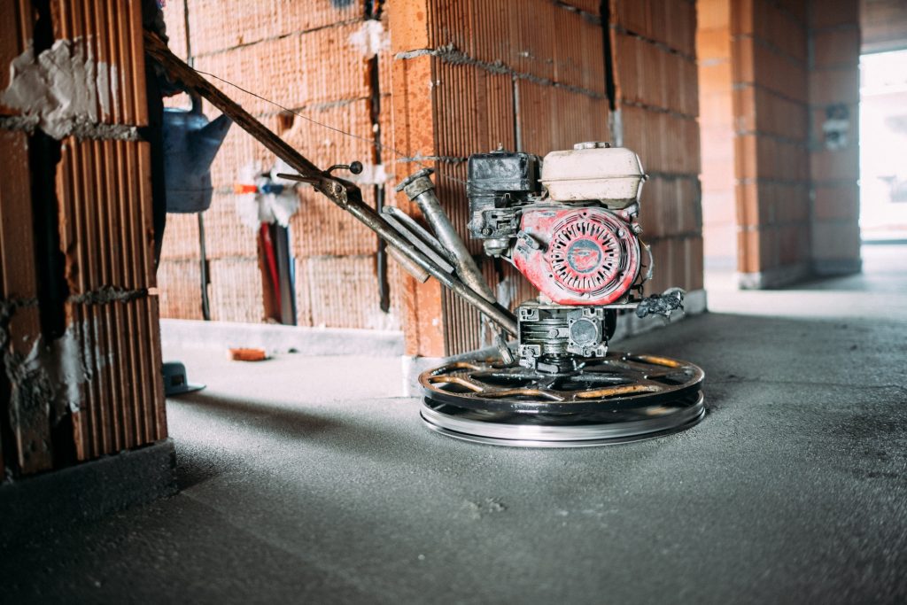 Construction worker finishing concrete screed with power trowel machine